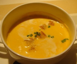 A bowl of pumpkin and bacon soup with croutons.10