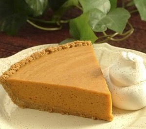 A wedge of pumpkin butterscotch pie on a plate with cream.