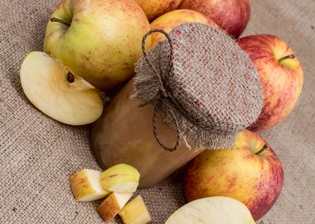 apples surrounding a bottle of apple sauce with a jute cover.