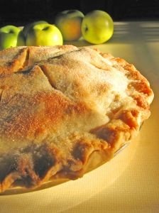 A freshly baked country apple pie with apples on the side.