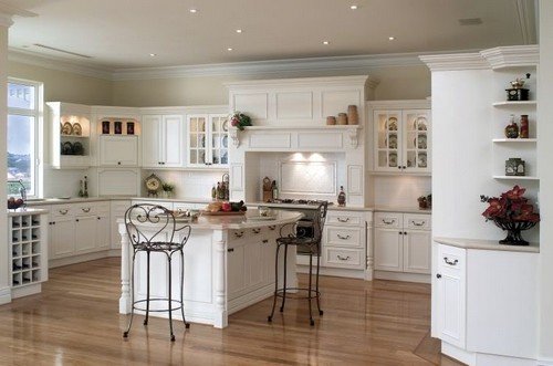 A French country kitchen with white cupboards and wooden floors.