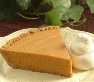 A wedge of pumpkin butterscotch pie on a plate with cream.