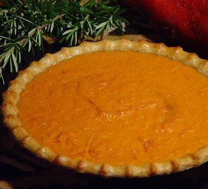 Pumpkin pie in a pie shell with rosemary on the side.