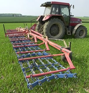 A tined weeder comb harrow being pulled by a tractor.